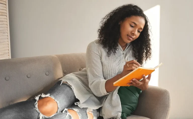 Woman writing in a journal while relaxing on a sofa at home