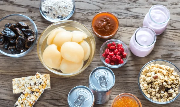 Yogurt, granola, cereal bars, dried fruit, sauces, and canned drinks arranged on a wooden table
