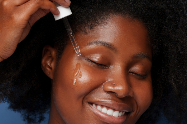 Black woman applying facial oil with a dropper to acne-prone skin with visible natural texture.