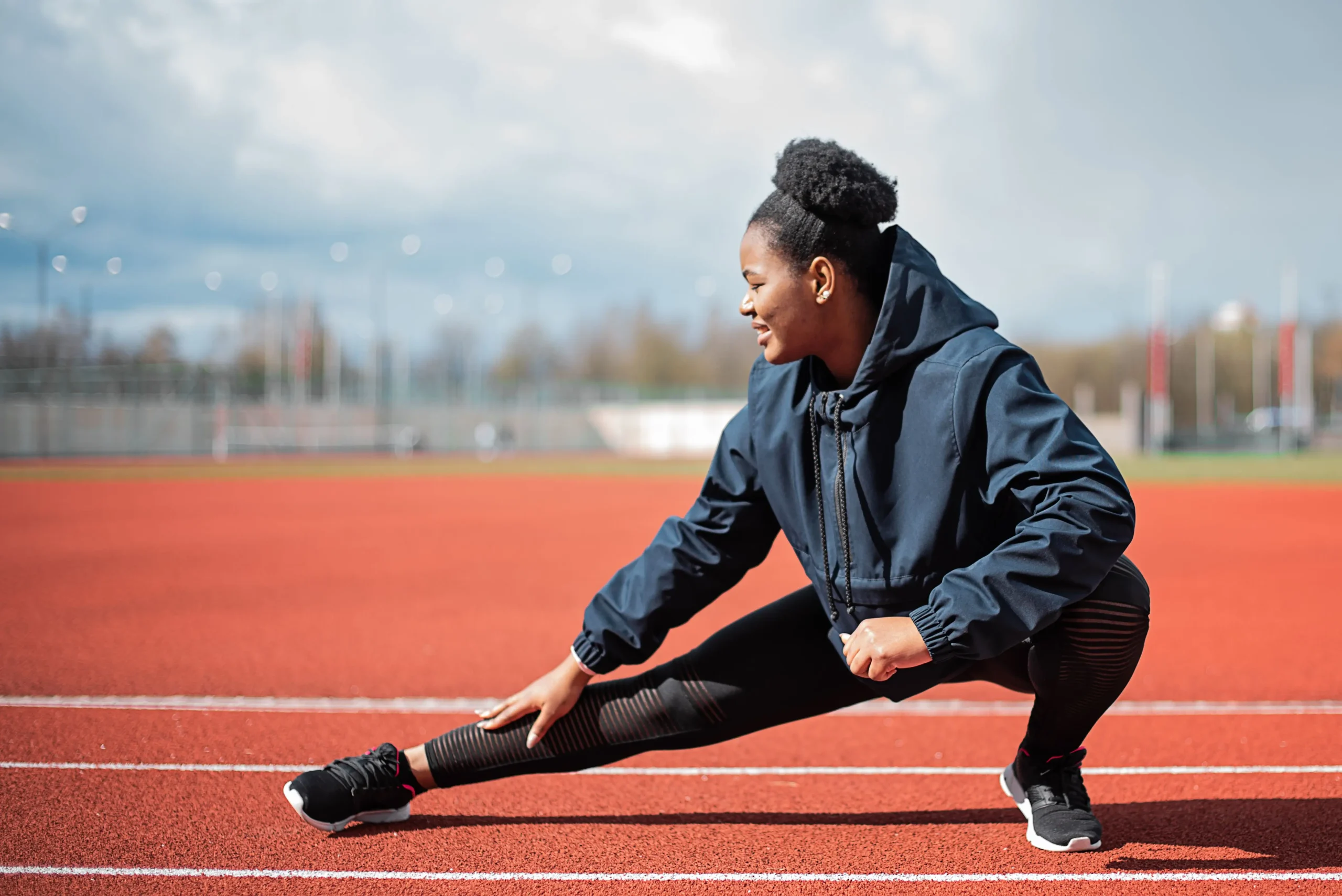Black woman stretching on an outdoor running track for an article about how exercise can benefit skin.