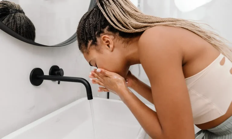 Woman washing her face at a sink as part of her skincare routine